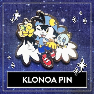 Könnte beinhalten: Eine goldfarbene Emaille-Anstecknadel mit einer Comicfigur namens Klonoa. Klonoa ist eine weiße und schwarze katzenartige Kreatur mit einem blauen Hut und einem gelben Stern. Klonoa hält einen gelben Stern und fliegt durch die Luft. Die Anstecknadel ist vor einem blauen Hintergrund mit weißen Sternen platziert.