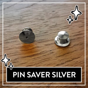 May include: Two silver pin savers, one with a flat top and the other with a round top, on a wooden surface.  PIN SAVER SILVER is written in white text on a black background.