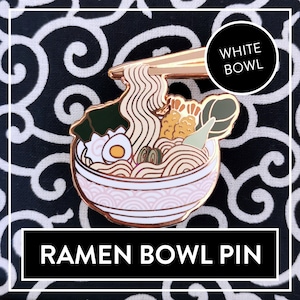 May include: A gold-tone enamel pin depicting a white ramen bowl with chopsticks lifting a noodle. The bowl has a pink and white wave pattern and is filled with noodles, an egg, seaweed, and other toppings. The pin reads "WHITE BOWL" and "RAMEN BOWL PIN".