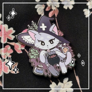 May include: A metal enamel pin featuring a light purple cat wearing a dark purple witch hat with a white cross symbol. The cat holds a small black cauldron and a glass potion bottle, surrounded by green foliage and a second potion bottle.