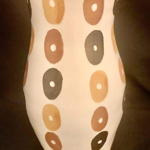 May include: White ceramic vase with a unique design featuring brown, orange, and black circles.