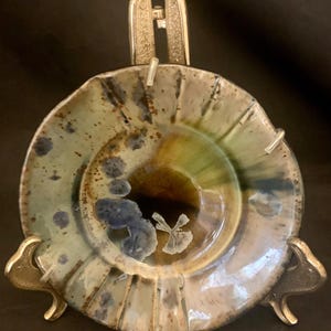 May include: A ceramic plate with a brown, green, and blue glaze. The plate has a wavy edge and is sitting on a gold metal stand.