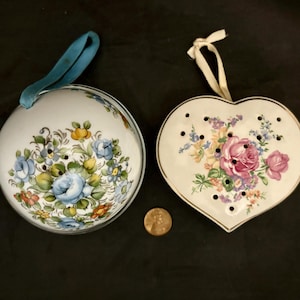 May include: Two vintage ceramic trinket dishes with floral designs. One is a round dish with a blue ribbon handle and the other is a heart-shaped dish.