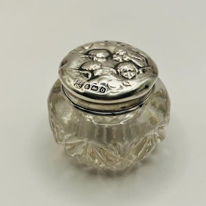 May include: A clear glass jar with a silver lid. The lid features a raised design of a tree and a bird. The jar is decorated with a cut glass pattern. The lid is hallmarked with the letters "BP DC" and the number "925".