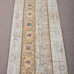 May include: A rectangular vintage rug with a patchwork design. The rug features a central panel in a warm yellow hue with floral motifs, flanked by panels in muted tones of beige and pastel colours. The rug has a distressed, antique appearance.