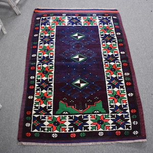 May include: A rectangular, hand-woven rug with a dark purple field and a detailed border. The border features a repeating pattern of white, red, green, and blue geometric shapes. The central design includes diamond and geometric shapes.