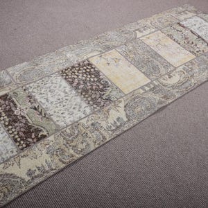 May include: Rectangular, patchwork-style rug with a neutral color palette. The rug features various rectangular panels in shades of beige, brown, and cream, with floral and geometric patterns. The rug is approximately 3 feet wide and 6 feet long.