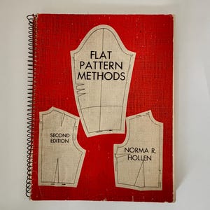 May include: A red spiral-bound book titled "Flat Pattern Methods" with illustrations of pattern pieces. The cover features the text "Second Edition" and the author's name, Norma R. Hollen. The book is designed for sewing and pattern making.