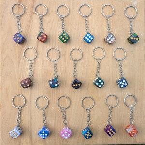 May include: A collection of 15 keychains with colorful dice charms. Each keychain has a silver ring and a silver chain. The dice are all different colors and patterns.