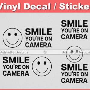 May include: Vinyl decal stickers with a smiley face and the text "SMILE YOU'RE ON CAMERA" in black. The stickers are in a variety of arrangements, with the text and smiley face in different positions.