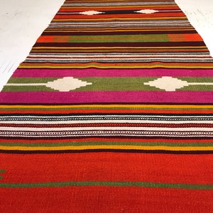 May include: A colorful woven rug with a geometric pattern in shades of red, orange, yellow, green, pink, and white.