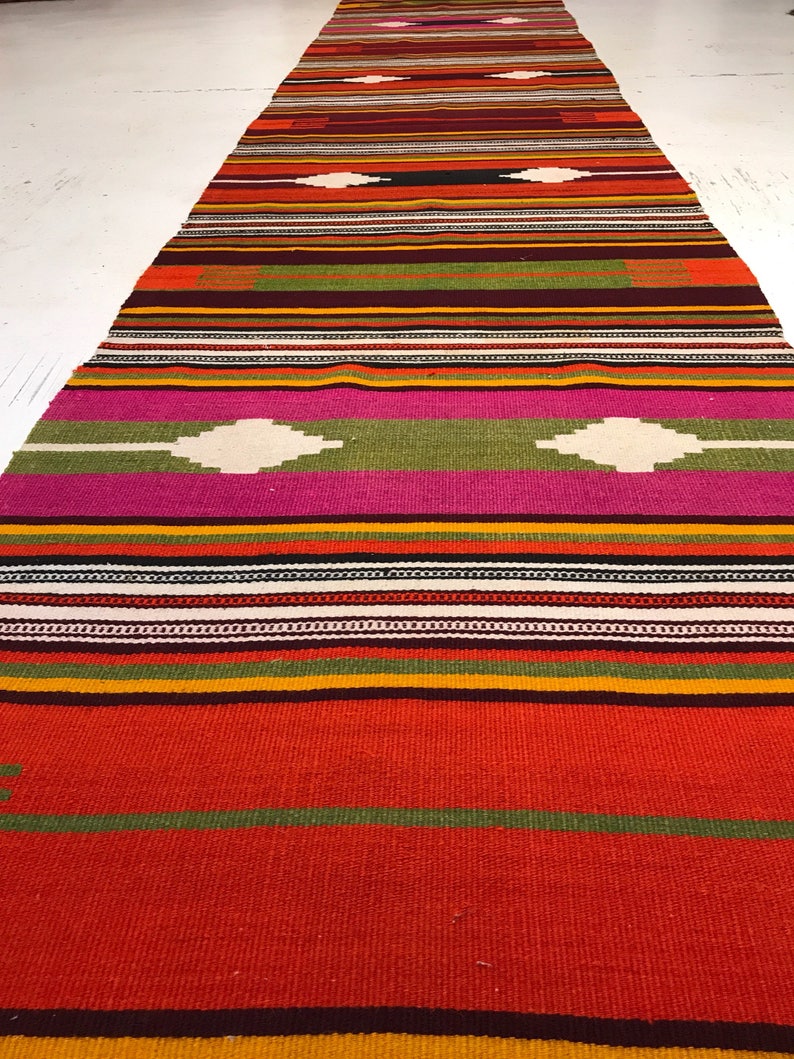 May include: A colorful woven rug with a geometric pattern in shades of red, orange, yellow, green, pink, and white.