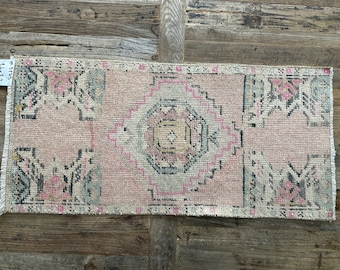 May include: A pink and white vintage rug with a geometric pattern. The rug has a faded look and is made of wool. The rug is approximately 2 feet by 3 feet.