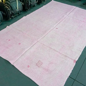 May include: A large, pale pink rug with a slightly rough texture. The rug has a few faint, darker pink spots.