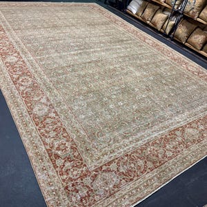 May include: A large, rectangular area rug with an intricate floral pattern in shades of beige, red, and cream. The rug features a detailed border with a repeating design. The rug is displayed on a dark surface.