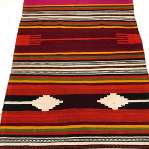 May include: A colorful striped rug with a geometric pattern. The rug is made of woven wool and has a variety of colors, including red, orange, yellow, green, black, and white.
