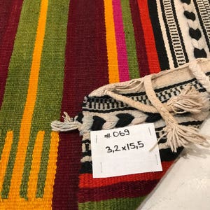 May include: A colorful striped woven rug with fringe. The rug is made of wool and has a geometric pattern. The rug is labeled #069 3.2 x 15.5.