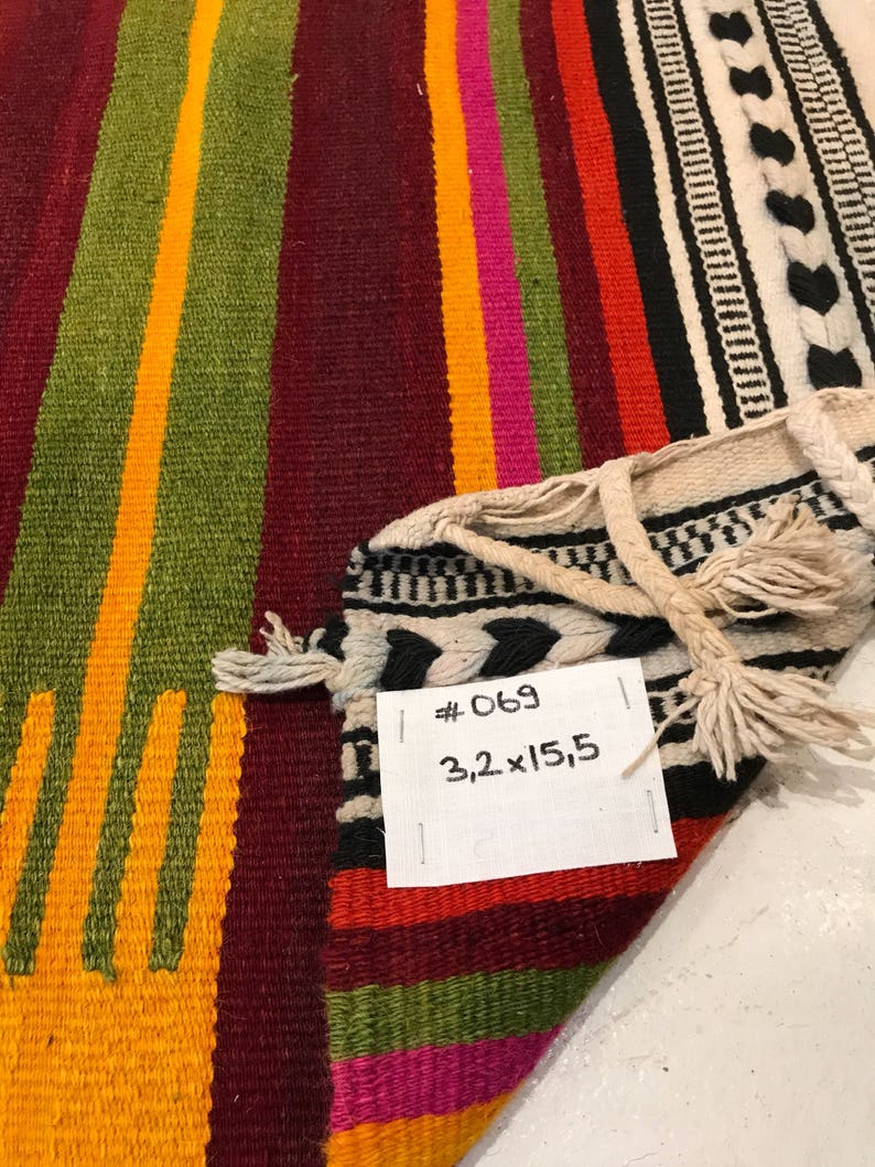 May include: A colorful striped woven rug with fringe. The rug is made of wool and has a geometric pattern. The rug is labeled #069 3.2 x 15.5.
