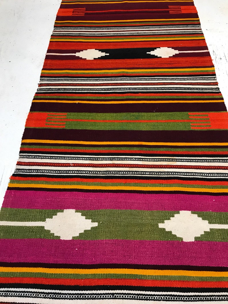 May include: A colorful striped rug with a geometric pattern. The rug is made of wool and has a traditional design. It is perfect for adding a touch of color and style to any room.
