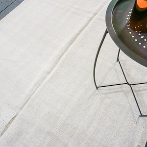 May include: A white rug with a black metal side table with a round tray and three legs. The tray has a pattern of small holes.