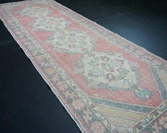 May include: A vintage runner rug with a faded pink and cream color scheme. The rug has a traditional floral pattern with a central medallion and a border.