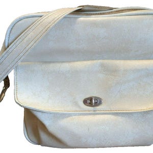 May include: A cream-colored shoulder bag with a subtle marbled texture, featuring a front flap pocket secured by a silver-toned metal turn-lock closure, a main zippered compartment, and an adjustable shoulder strap attached to the sides.