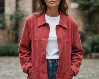 Può includere: Giacca di velluto a coste rossa con bottoni, due tasche frontali e colletto. Indossata sopra una maglietta bianca e jeans blu. Lo sfondo presenta un edificio con fogliame verde.