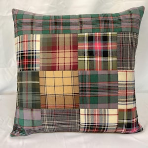 Può includere: Cuscino decorativo quadrato con un design patchwork. Il cuscino presenta vari motivi scozzesi in tonalità di verde, rosso, giallo e grigio. Il cuscino è di forma quadrata e sembra essere fatto di tessuto.