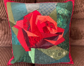 May include: A red, green, and white patchwork pillow with a large red rose design. The rose is made of many different fabric pieces sewn together.
