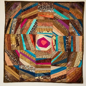 Peut inclure: Une courtepointe circulaire avec un motif de patchwork brun, beige et turquoise. Le centre de la courtepointe présente une forme de diamant rose et rouge.