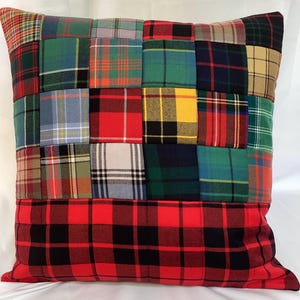 May include: Square patchwork pillow with a variety of plaid patterns in red, green, blue, yellow, and black. The bottom section features a large red and black plaid design. The pillow is a decorative home accent.