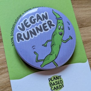 Può includere: Un bottone viola e verde con il testo "VEGAN RUNNER" e un fagiolino verde dei cartoni animati che corre. Il bottone è 100% biodegradabile e sul retro dice "PLANT BASED CARDS by Dan plantbasedcards.co.uk @Plantbasedcards".