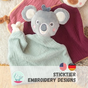 May include: A gray plush koala head with a light blue fabric body, set against a pink and burgundy background. The koala has white accents on its ears and a small blue tuft. The text "STICKTIER EMBROIDERY DESIGNS" is at the bottom.