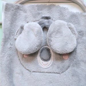 May include: A gray plush koala face with embroidered details, including a nose, eyes, and ears. The koala is part of a larger fabric piece, possibly for a baby item. The design is in an embroidery hoop.