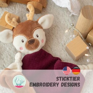 Può includere: Un giocattolo di peluche a forma di cervo con testa marrone, orecchie color crema e corpo bordeaux. Il cervo ha tratti del viso ricamati e piccole corna. Il testo "STICKTIER EMBROIDERY DESIGNS" è visualizzato sotto.