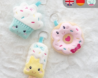 May include: Three plush keychains shaped like a cupcake, donut, and popsicle. The cupcake is light blue and white with pink frosting and sprinkles. The donut is pink with white frosting and sprinkles. The popsicle is yellow with white frosting and sprinkles.