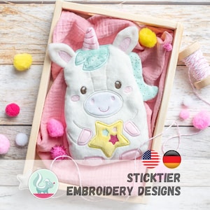 May include: A soft white unicorn toy with a pink horn and star design, displayed in a wooden box with pink fabric and colourful pom-poms. The text "STICKTIER EMBROIDERY DESIGNS" is visible.