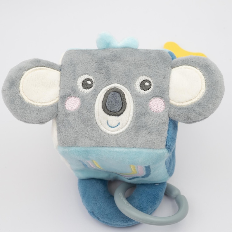 May include: A plush, gray koala-shaped baby toy with a blue bow, large ears, and a smiling face. The toy has a blue base with a ring and a soft, textured feel, designed for infants.