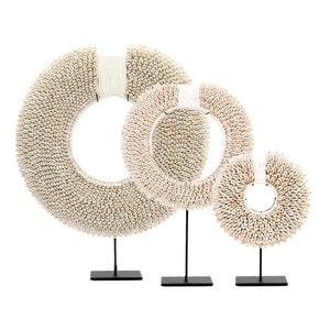 May include: Three white shell wreaths on black metal stands. The wreaths are different sizes and are made of small, white shells.
