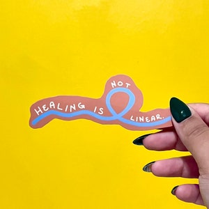 May include: A sticker with a blue line that curves into a loop, with the words "HEALING IS NOT LINEAR." The sticker is on a yellow background.