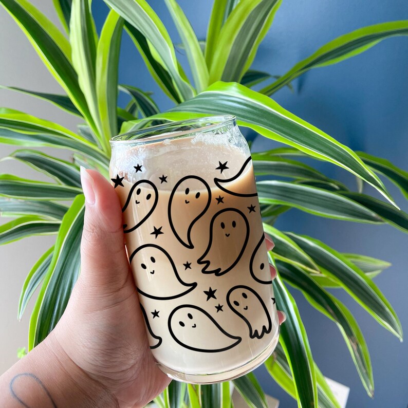 Puede incluir: Una lata de vidrio transparente con un l&iacute;quido marr&oacute;n en su interior. La lata tiene un patr&oacute;n de fantasmas y estrellas en blanco y negro.