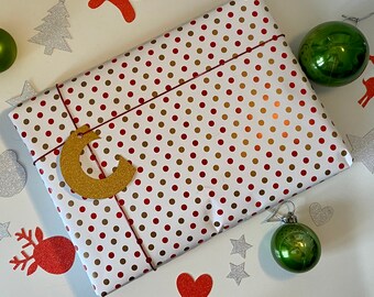 May include: A white and red polka dot gift wrap with a gold glitter letter C on it. The gift wrap is surrounded by Christmas decorations, including a green ornament, a red and white candy cane, and a white snowflake.