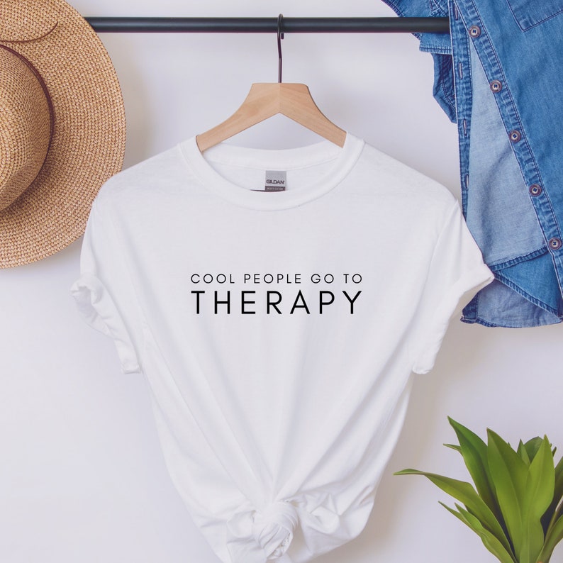 May include: White t-shirt with black text that reads "Cool People Go To Therapy".