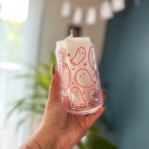 Puede incluir: Un vaso de vidrio transparente con un dise&ntilde;o de fantasmas rosas. El vaso tiene un contorno rosa de fantasmas con estrellas y una servilleta de papel blanca en su interior.