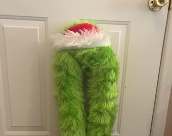 Puede incluir: Piernas de Grinch peludas de color verde con zapatos rojos y un ribete de piel blanca. Las piernas están de pie con los zapatos rojos apuntando hacia adelante.