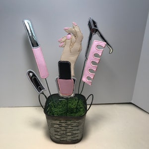 K&ouml;nnte beinhalten: Ein Metalleimer gef&uuml;llt mit gr&uuml;nem Moos, obenauf eine Hand und verschiedene Nagelpflegewerkzeuge, darunter eine Nagelfeile, Nagelknipser und Nagellack.