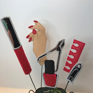 K&ouml;nnte beinhalten: Ein Set aus f&uuml;nf Filz-Dekorationen zum Thema Nagelstudio. Die Dekorationen umfassen eine Nagelfeile, einen Nagelknipser, eine Flasche Nagellack, eine Hand mit rotem Nagellack und eine Tube roten Nagellacks.