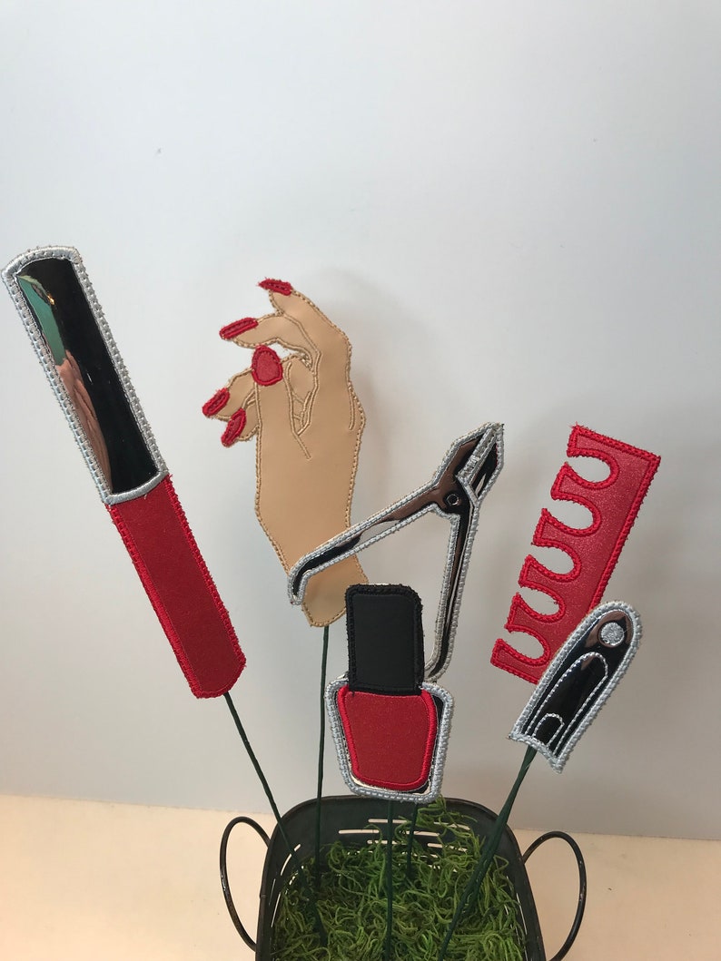 K&ouml;nnte beinhalten: Ein Set aus f&uuml;nf Filz-Dekorationen zum Thema Nagelstudio. Die Dekorationen umfassen eine Nagelfeile, einen Nagelknipser, eine Flasche Nagellack, eine Hand mit rotem Nagellack und eine Tube roten Nagellacks.