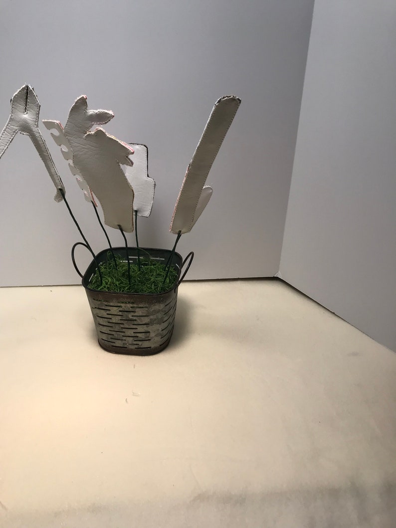 K&ouml;nnte beinhalten: Ein kleiner Metalleimer mit gr&uuml;nem Moos drinnen. F&uuml;nf wei&szlig;e Papierformen sind an Dr&auml;hten befestigt und ragen aus dem Moos heraus. Die Formen sind in verschiedenen Gr&ouml;&szlig;en und Formen.
