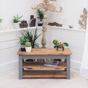 May include: A gray wooden shelf unit with two shelves. The shelf unit has a natural wood top and gray painted legs and shelves. The shelf unit is sitting on a wooden floor. There are books and a small wooden horse figurine on the shelves.